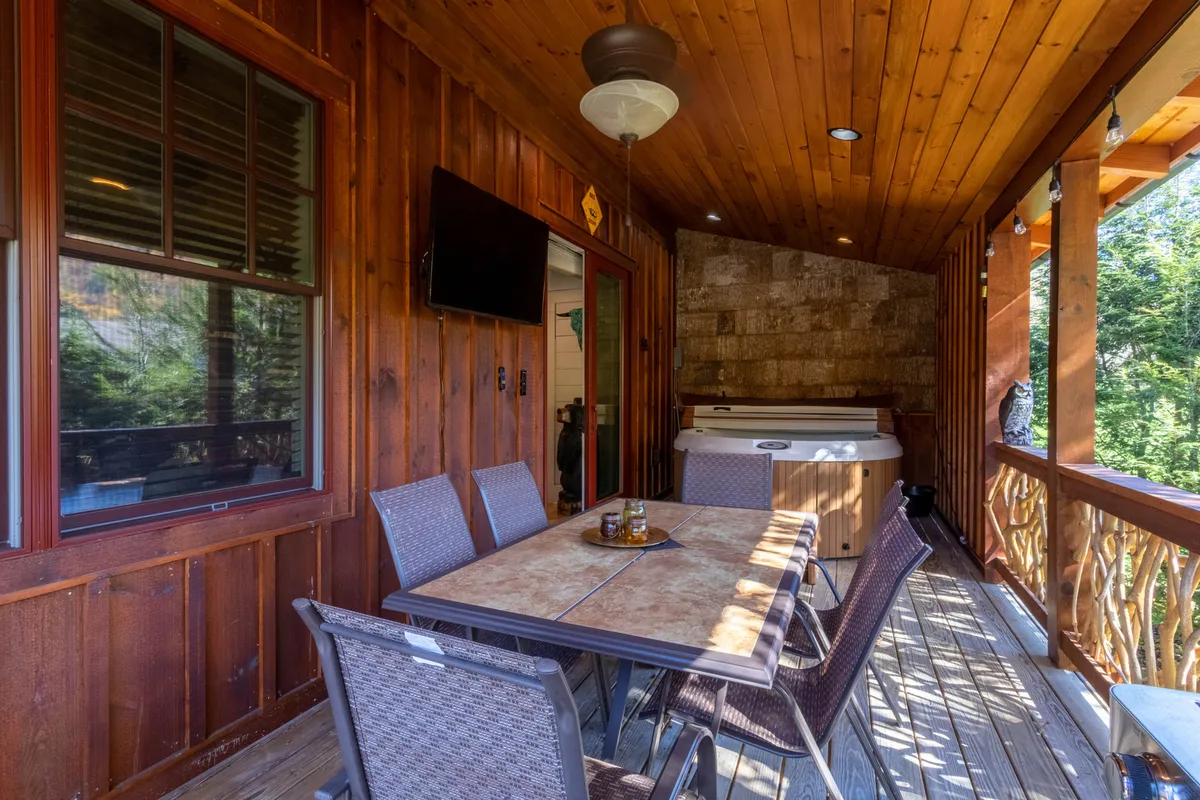 This image presents another angle of a comfortable outdoor space, focusing on a dining table and hot tub on a porch-like area. The scene is framed with warm wooden walls and a ceiling fan, emphasizing comfort and relaxation for gatherings, sunset dinners, or stargazing.
