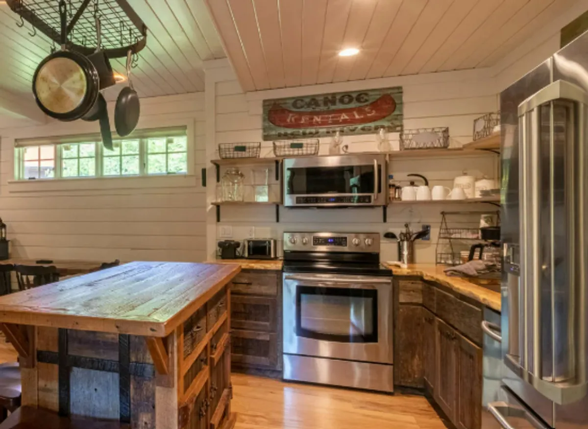 A well-appointed kitchen showcasing a prominent granite island, stainless steel appliances, open shelving, and a hanging pot rack. The cozy touches and clear workspace make it ideal for cooking and gathering.