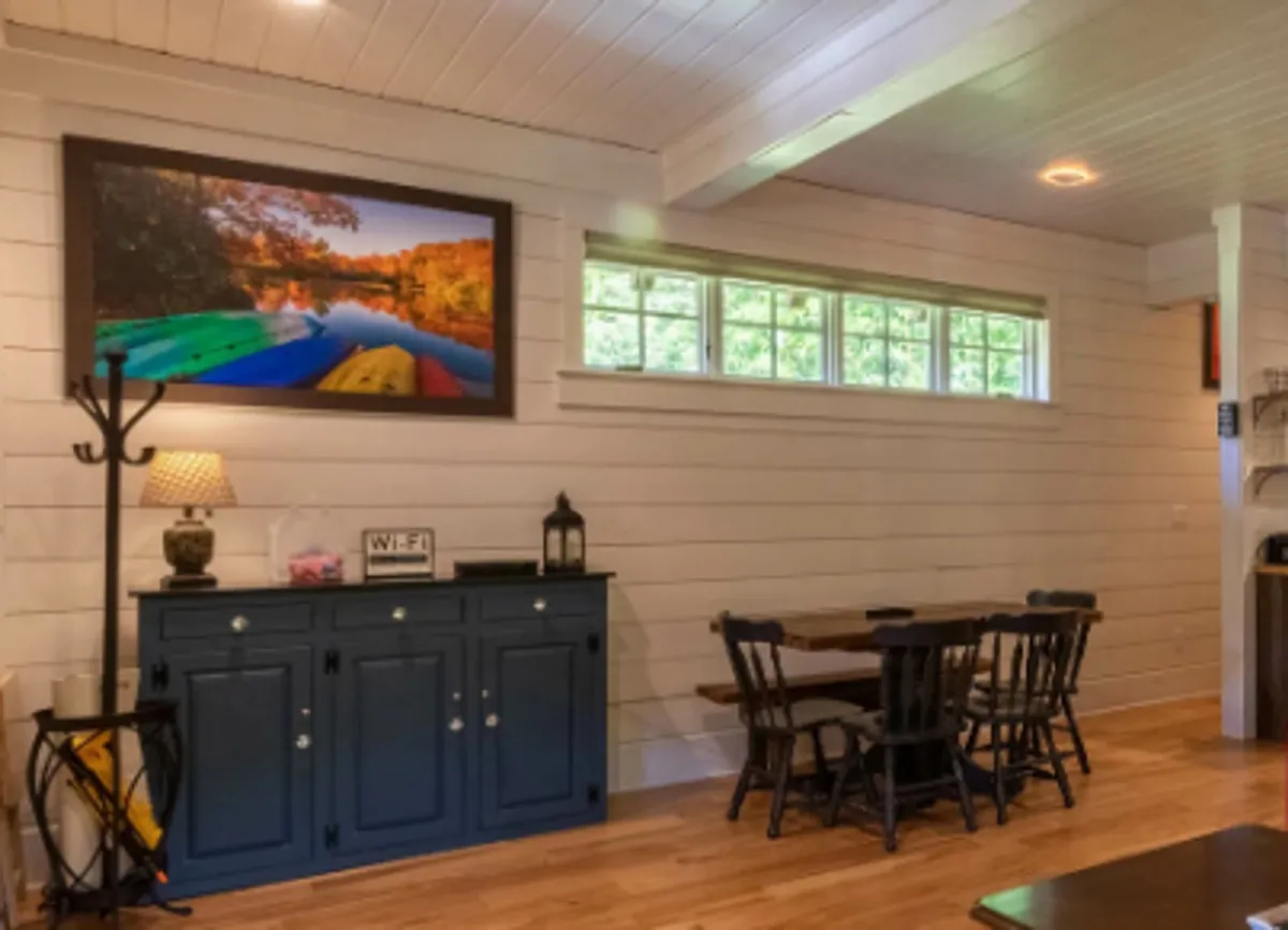 A warmly lit interior scene featuring a dining table with colorful artwork on the walls and a blue storage cabinet. The space feels functional yet vibrant, highlighting practical living areas adjacent to social zones.
