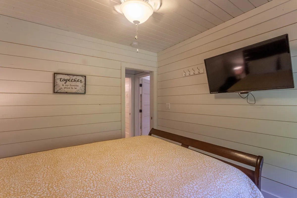 A guest bedroom with a full-sized bed adorned in patterned bedding, a flat-screen TV mounted on the wall, and a decorative wall sign. The setting feels welcoming and comfortable, ideal for children or another couple.
