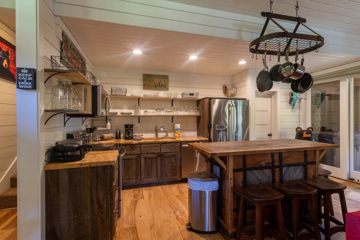 A cozy kitchen scene with a wooden bar counter, stainless steel refrigerator, and open shelving displaying glassware and cookware. The setting is organized and polished, reinforcing the theme of stylish, practical amenities.